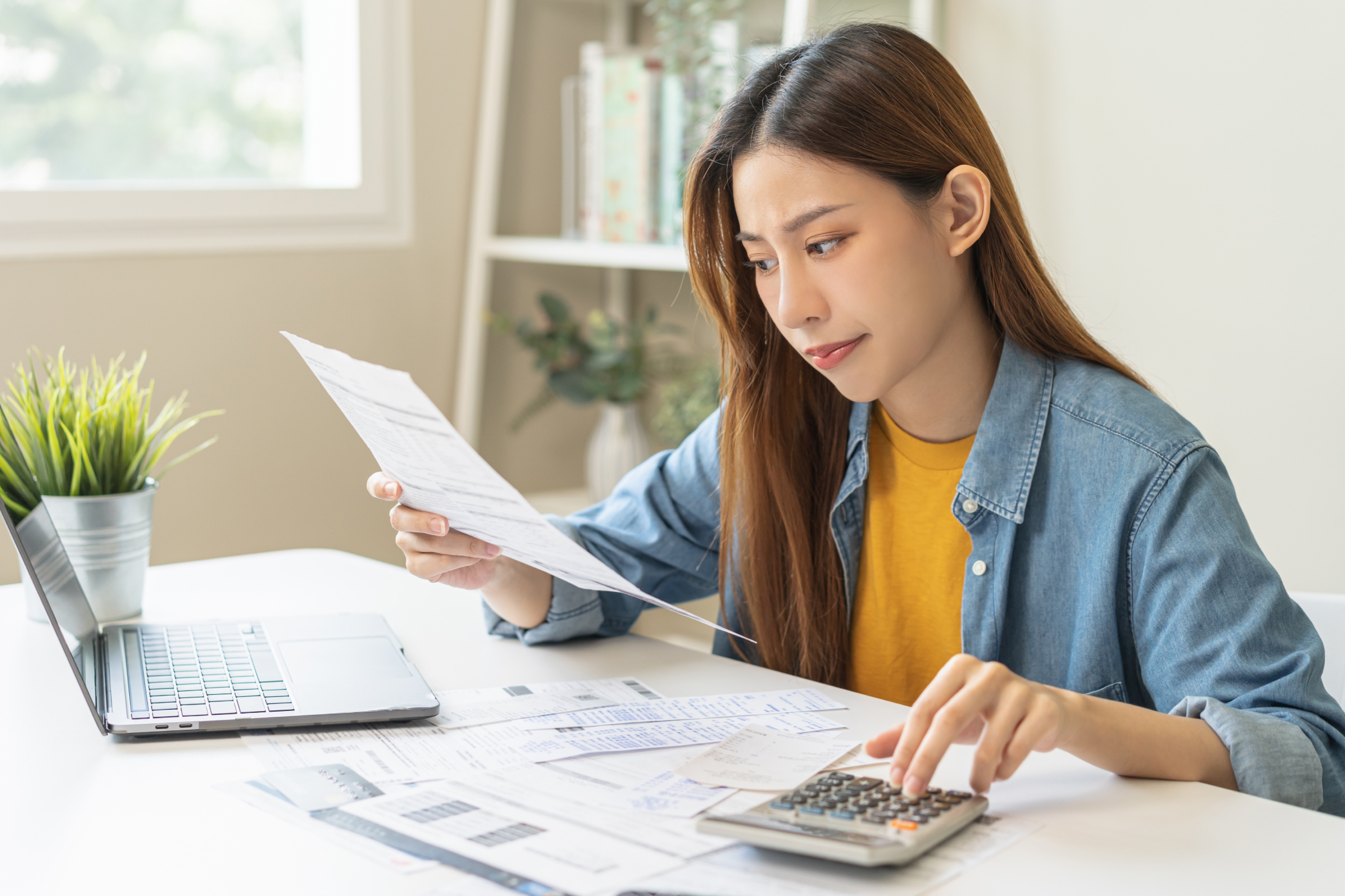 Woman reviewing documents and using a calculator at her laptop.